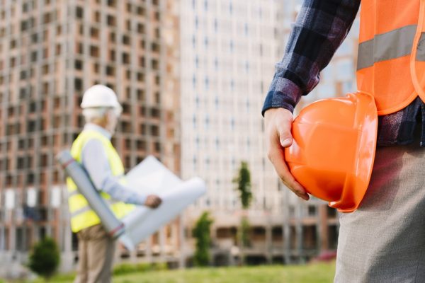 Homem segurando um capacete de segurança em frente a um prédio